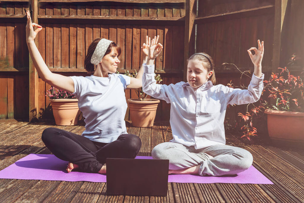 Glückliche Mutter und Tochter machen Online-Yoga mit Laptop während der Selbstisolierung im Garten, kein Gerätetraining, Meditationstipps für Anfänger, zu Hause bleiben und gesund bleiben Konzept - Foto, Bild
