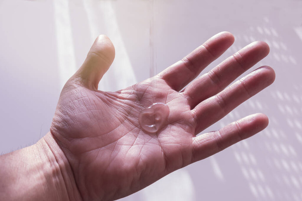 Een man die hydroalcoholische desinfecterende gel gebruikt, die uit een fles op zijn hand valt. Achterlicht van de zon - Foto, afbeelding