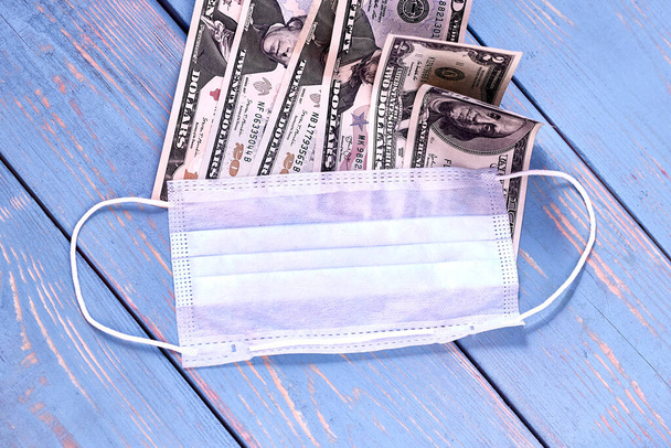 Fondo de madera en estilo retro en color azul. Lleva una máscara médica y billetes, dólares. Concepto de aumento de los precios de los servicios
 - Foto, imagen