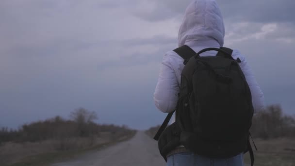 free girl traveler with a backpack in protective medical mask and hood is walking out of town on road. Protection against viruses and bacteria. health and safety concept, coronavirus N1H1, virus - Filmagem, Vídeo
