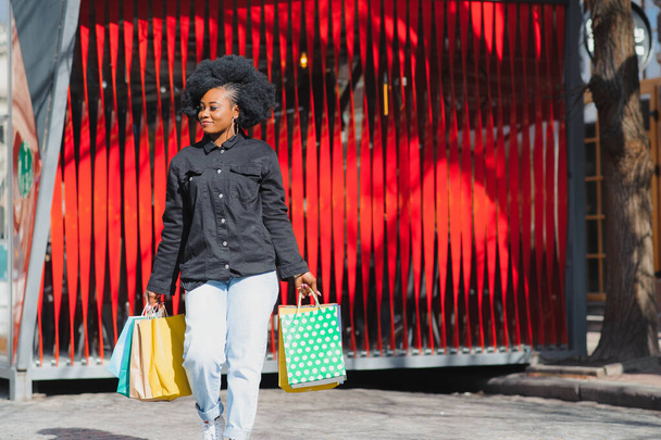Portrait beautiful smiling african woman with shopping bags in city over red background - Foto, immagini