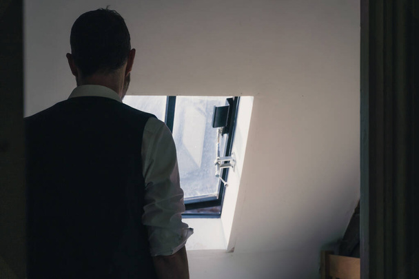 A man looking out of a window, back to camera, wearing a waistcoat - Photo, Image