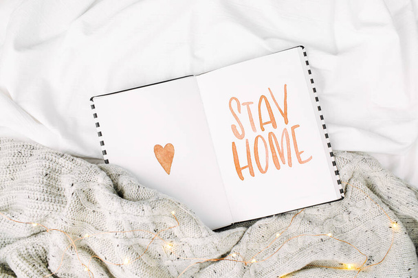 Stay Home, quarantine. Open   planner with warning on bed with warm plaid. Copy space. Flat lay, top view - Fotografie, Obrázek
