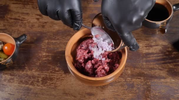 Küche im Restaurant, Food-Video, Zeitlupe. Nahaufnahme eines männlichen Kochs in schwarzen Handschuhen, der ein Gourmetgericht mit Fleischtartar zubereitet und Salatzutaten in einer Schüssel mixt. Volle Konzentration - Filmmaterial, Video