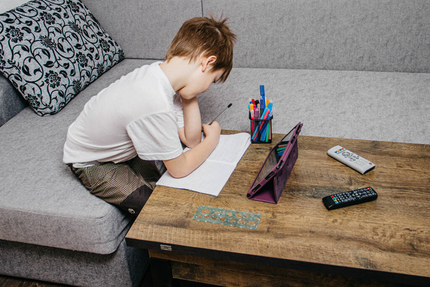 Ένα αγόρι κάθεται στο σπίτι στην απομόνωση και μαθαίνει στο διαδίκτυο - Φωτογραφία, εικόνα