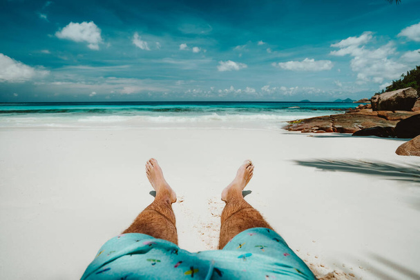 Male in swimming shorts resting on pure white sand beach with beautiful blue ocean lagoon view - 写真・画像