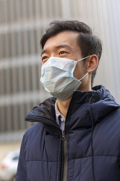 Hombre chino con máscara médica contra 2019-nCov mirando hacia otro lado. Al aire libre
 - Foto, Imagen