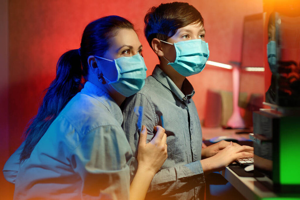 Ritratto di madre e figlio, indossare una maschera protettiva, cercando di difendersi da un'epidemia, coronavirus. imparare lezioni online su un computer
. - Foto, immagini