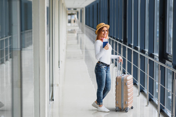 Valmiina matkaan. Nainen pitää passia kädessä matkatavaroiden kanssa lentokentän taustalla. Huippusesonki ja loma käsite. Rentoudu ja elämäntavat
 - Valokuva, kuva