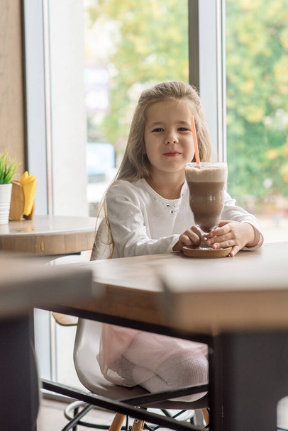 Funny girl 5 years old drinks hot chocolate with marfmellow in a cafe - Foto, Imagen