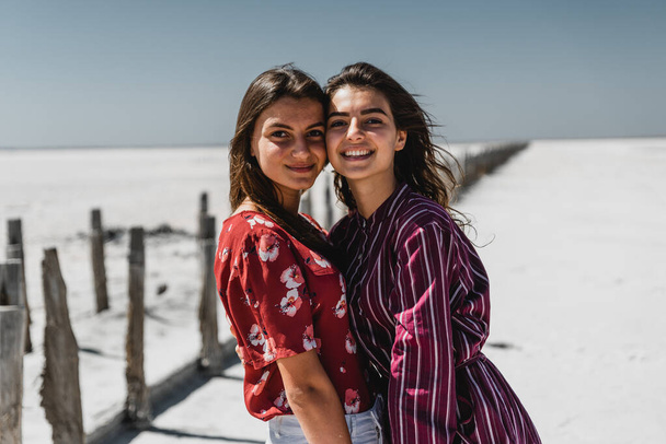 happy girlfriends stand and hug in nature,stylishly dressed young european girls,young girls walk on a hot summer day,young people on a beautiful background,happy girls smile and enjoy life,sisters cuddle,young and happy best friends,best friends wom - Fotografie, Obrázek