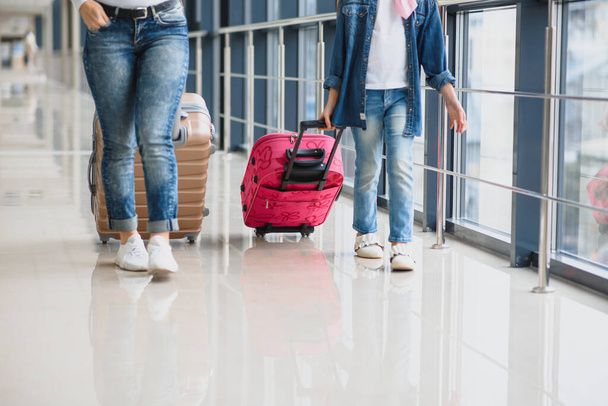 Happy young mother and her daughter walking in the airport terminal while carrying a suitcase. High season and vacation concept. Relax and lifestyles - Photo, Image