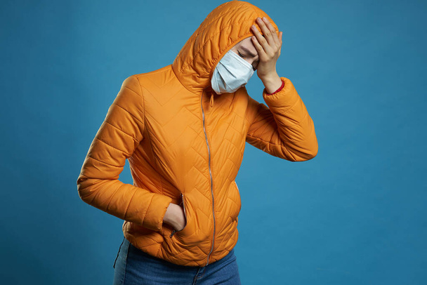 woman wearing hood in a protective face mask and coat over blue background. Model girl in medical mask and spring outfit, studio shot with copy space for your text. Anti-flu, anti-epidemic - Foto, Imagem