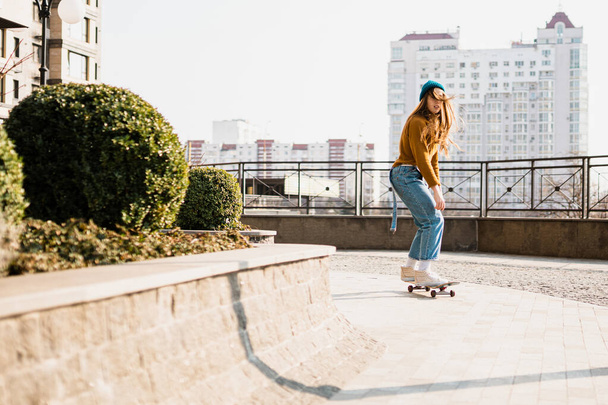 Skateboard Femme dans la ville. Skater girl en denim monte sa planche sur la place. Femme athlétique skateboarder. Bâtir sur l'arrière-plan. Concept d'activités de loisirs, urbaines et sportives
. - Photo, image