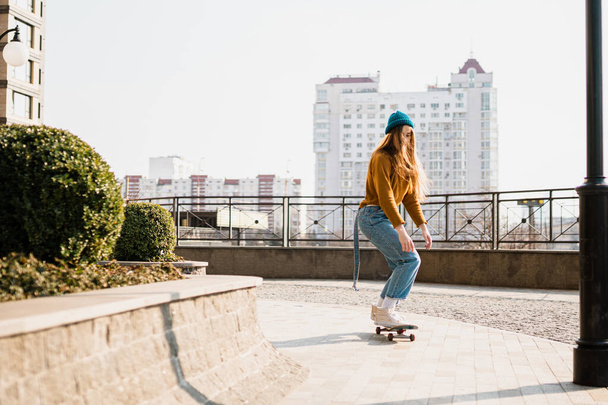 Joven mujer guapa montando en un monopatín. Retrato de modelo deportivo femenino en estilo urbano. Skateboarding en la ciudad. Traje de calle. Mujer urbana montada en patín. Hipster chica en el monopatín
. - Foto, imagen