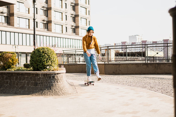 Young handsome woman riding on a skateboard. Portrait of sport female model in urban style. Skateboarding at city. Street style outfit. Urban woman ride on skate. Hipster girl on skateboard. - Photo, Image