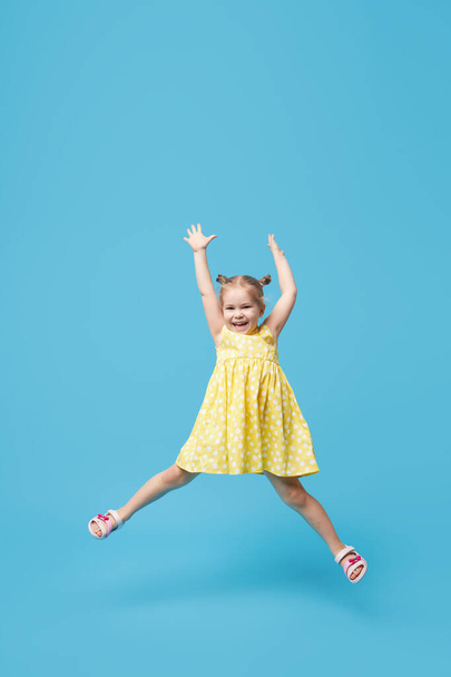 Portrait of smiling cute little toddler girl. child jumping isolated over blue background. Looking at camera and laughs - 写真・画像
