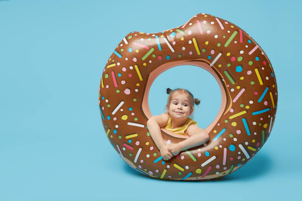 Failed summer vacation. Happy surprised toddler girl resting on a donut-shaped rubber ring. Sea vacation concept on a colored blue background. Wow emotions	 - Foto, imagen