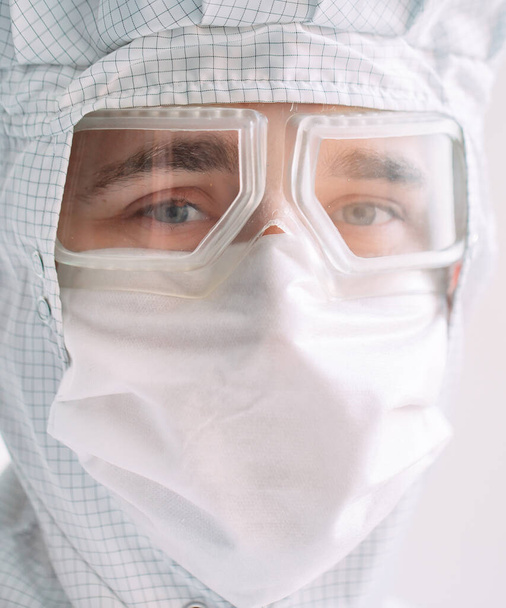 Retrato de um médico masculino de aparência europeia em uma máscara médica, óculos de proteção e terno químico - Foto, Imagem