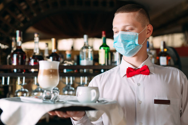 A European-looking waiter in a medical mask serves Latte coffee - Fotografie, Obrázek