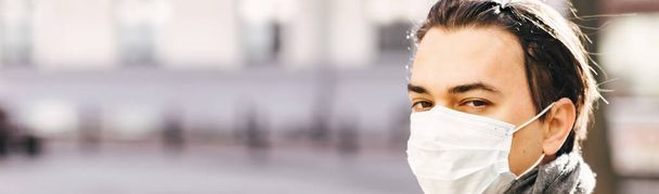 Mann mit Schutzmaske läuft in Quarantäne-Stadt. Kerl mit medizinischer Maske auf dem Gesicht blickt in die Kamera. Coronavirus. Virenschutz. Seuchenepidemie. Banner - Foto, Bild