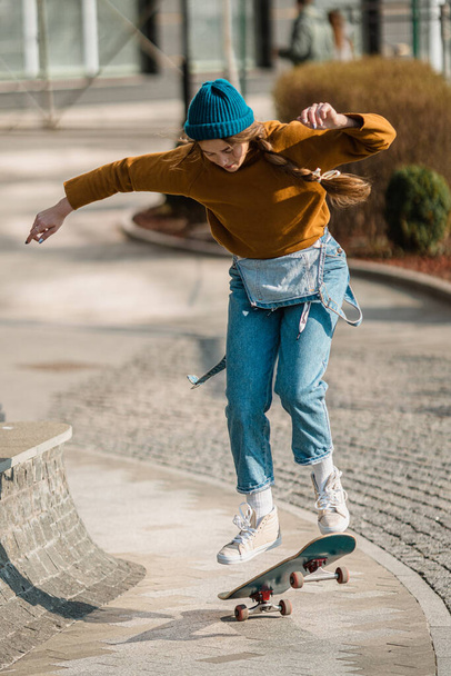 Young handsome woman riding on a skateboard. Portrait of sport female model in urban style. Skateboarding at city. Street style outfit. Urban woman ride on skate. Hipster girl on skateboard. - Foto, afbeelding