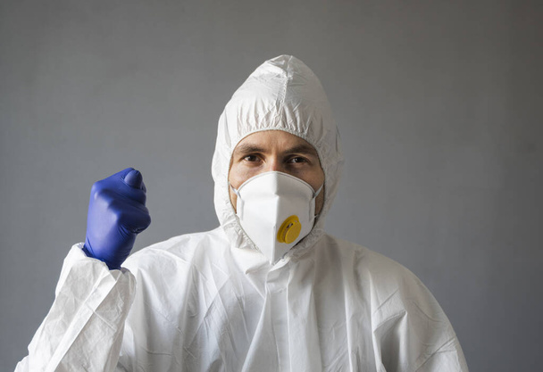 Doctor in white protective suit, medical mask and rubber gloves is showing Fig sign to the virus. Helping a people while coronavirus pandemic threat. Epidemic, pandemic of coronavirus covid 19. - Foto, Imagem
