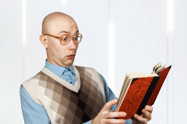 Portrait Young bald guy mad in glasses reading book and surprised - Фото, изображение