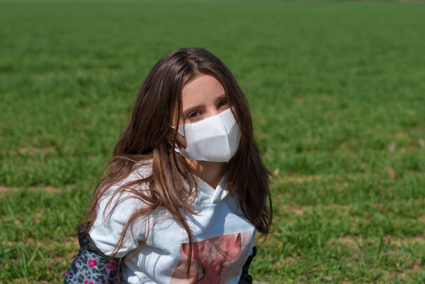Mädchen mit Schutzmaske auf dem Gesicht in der Natur an einem sonnigen Tag. Schutzmasken vor Coronavirus. - Foto, Bild