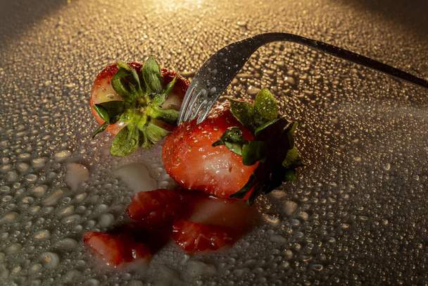 Fourchette piquant une fraise avec des gouttes d'eau et incident léger
. - Photo, image