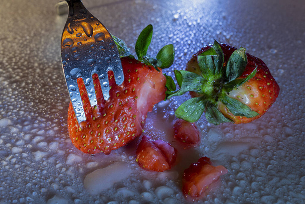 Fourchette piquant une fraise avec des gouttes d'eau et incident léger
. - Photo, image