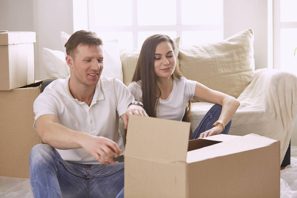Portrait of happy couple looking at laptop computer together sitting in new house, surrounded with boxes - Photo, image