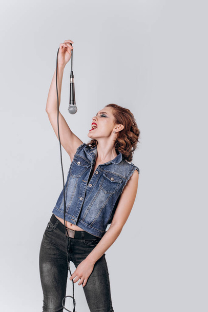 A beautiful girl with a microphone sings on an isolated white background - Zdjęcie, obraz
