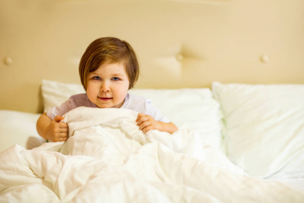 a sweet little girl with blue eyes ,lying in a white bed, under quarantine because of the covid-19 pandemic - Photo, Image