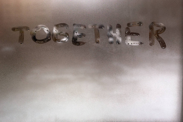 das Wort zusammen handgeschrieben auf feuchtem Fensterglas bei Tag - Nahaufnahme Vollbild mit selektivem Fokus und Hintergrundunschärfe - Foto, Bild