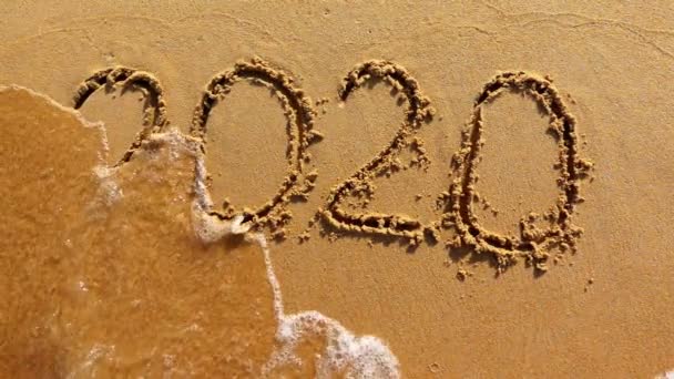 Woord 2020 jaar geschilderd op het zand wordt weggespoeld door de golf - Video