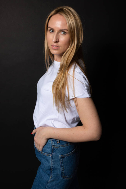 Beautiful young woman poses looking at camera. Hands in pocket. Black backgroung - Foto, immagini