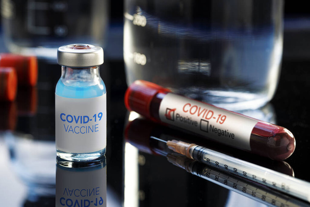Covid-19 Written vaccine bottle with a blue liquid, a syringe and a blood sample on a laboratory like background. - Φωτογραφία, εικόνα