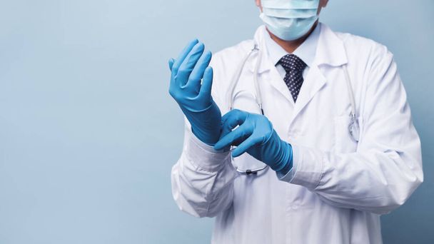 Врач в медицинской маске надевает резиновые перчатки. средства от инфекции и короновируса
 - Фото, изображение