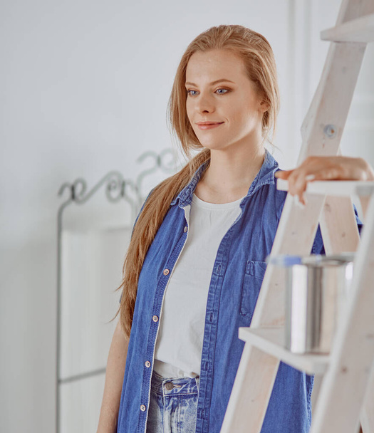 Piękna młoda kobieta na białym drewnianym drabinie. Gotowy do naprawy pokoju. Koncepcja prac domowych dla kobiet - Zdjęcie, obraz