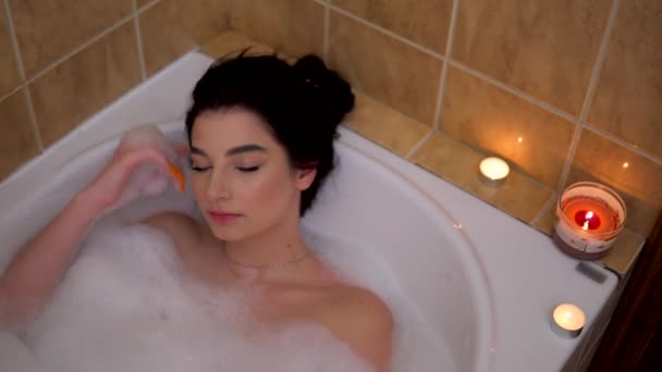 Mladá žena relaxace v bublinkové koupeli se svíčkami, útulná romantická atmosféra - Záběry, video