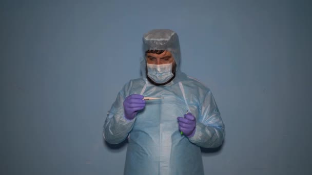 Ein bärtiger Arzt zieht während der Covid-19-Coronavirus-Pandemie in einem Labor einen medizinischen Schutzanzug an. - Filmmaterial, Video