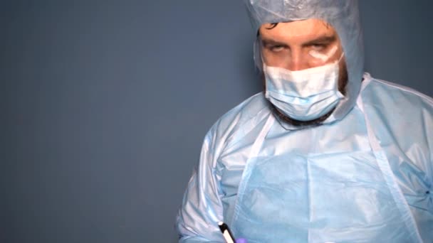 Koruyucu giysili sakallı bir doktor Covid-19 Coronavirus salgını sırasında laboratuvar şişelerini analiz için kontrol ediyor. Sisli maskeli yorgun doktor. - Video, Çekim
