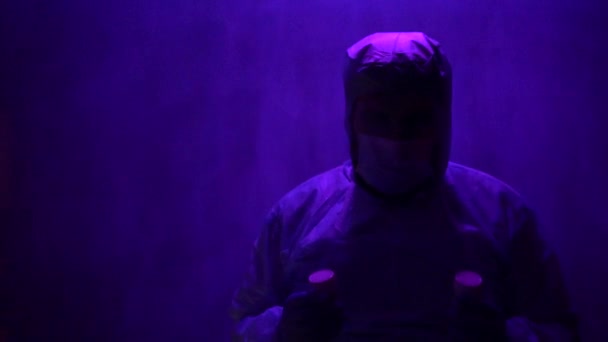 Un médico barbudo con traje protector revisa los frascos de laboratorio para su análisis durante la pandemia del coronavirus Covid-19. Médico cansado con una máscara de niebla
. - Imágenes, Vídeo