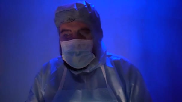 Baard arts in een beschermende medische pak tijdens angst in het laboratorium. Ongeval in het laboratorium tijdens de coronaviruspandemie. Het licht van de sirene is blauw-rood. Het effect van slechte verlichting in de ruimte. - Video
