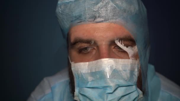 Ein müder bärtiger Arzt atmet in eine Nebelmaske und blickt in die Kamera. Nahaufnahme. Schweiß fließt beim Atmen die medizinische Maske hinunter. - Filmmaterial, Video
