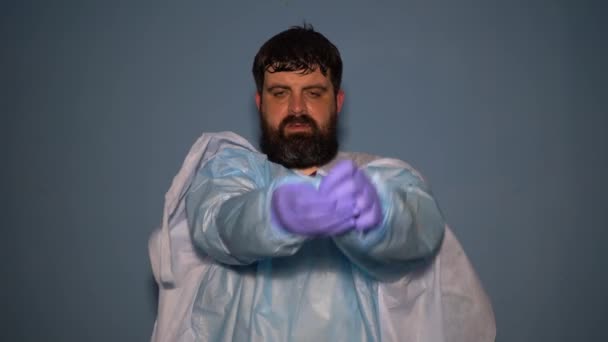 Un dottore stanco si toglie la sua tuta protettiva durante una pandemia di coronavirus. Un medico sudato rimuove una maschera medica e guanti alla fine del turno
. - Filmati, video