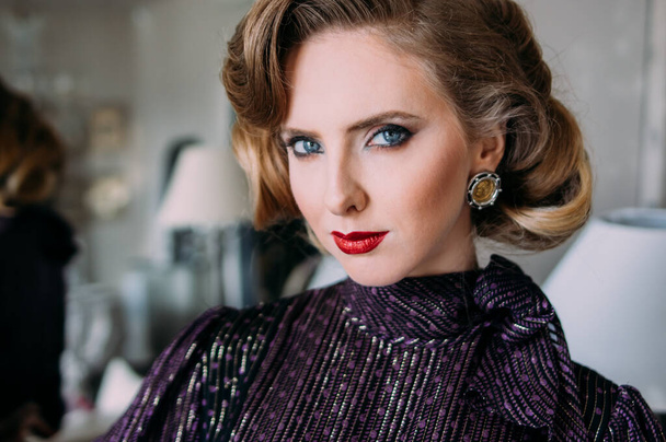 Portrait of beautiful blond girl with vintage make up and hairstyle weared in retro purple dress and looking to camera - Foto, Imagem