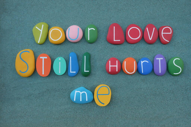 Your love still hurts me, phrase composed with multi colored stone letters over green sand - Foto, afbeelding