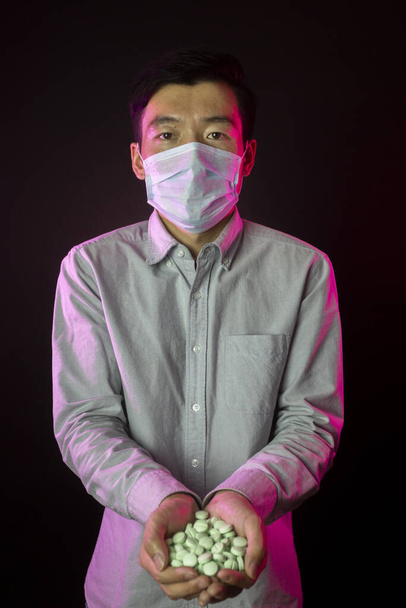 Ázsiai férfi arcpakolásban 2019-nCov ellen, maroknyi pirulával. Fekete háttér - Fotó, kép
